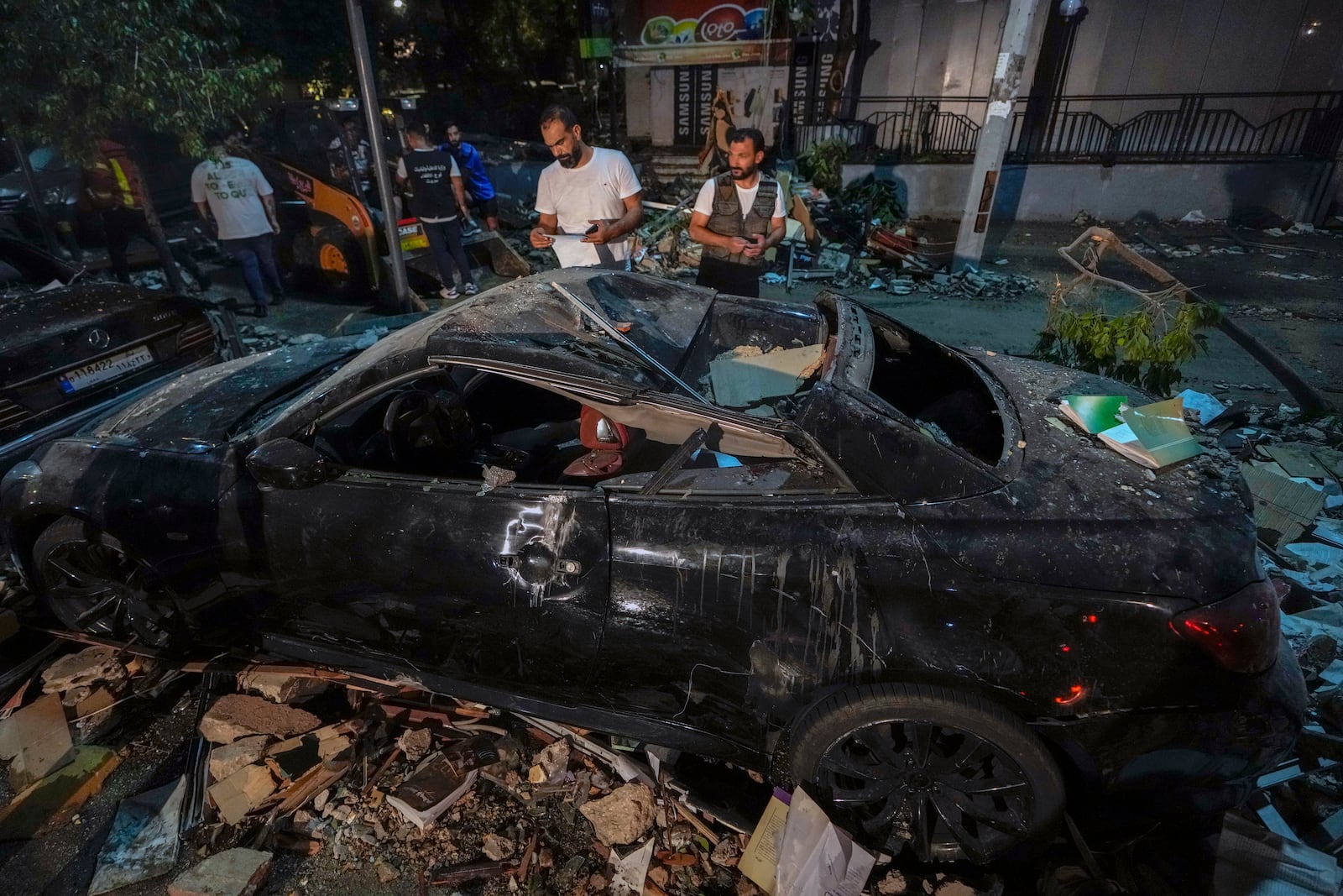 People inspect a damaged car near a building that was hit in an Israeli airstrike, in Beirut, Lebanon, early Monday, Sept. 30, 2024. (AP Photo/Bilal Hussein)