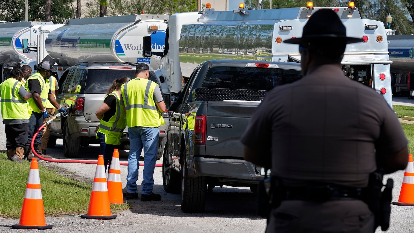 A Florida Highway Patrol officer watches as fuel depot workers distribute gas to residents Saturday, Oct. 12, 2024, in Plant City, Fla. Gas stations are slow to reopen after the effects of Hurricane Milton. (AP Photo/Chris O'Meara)