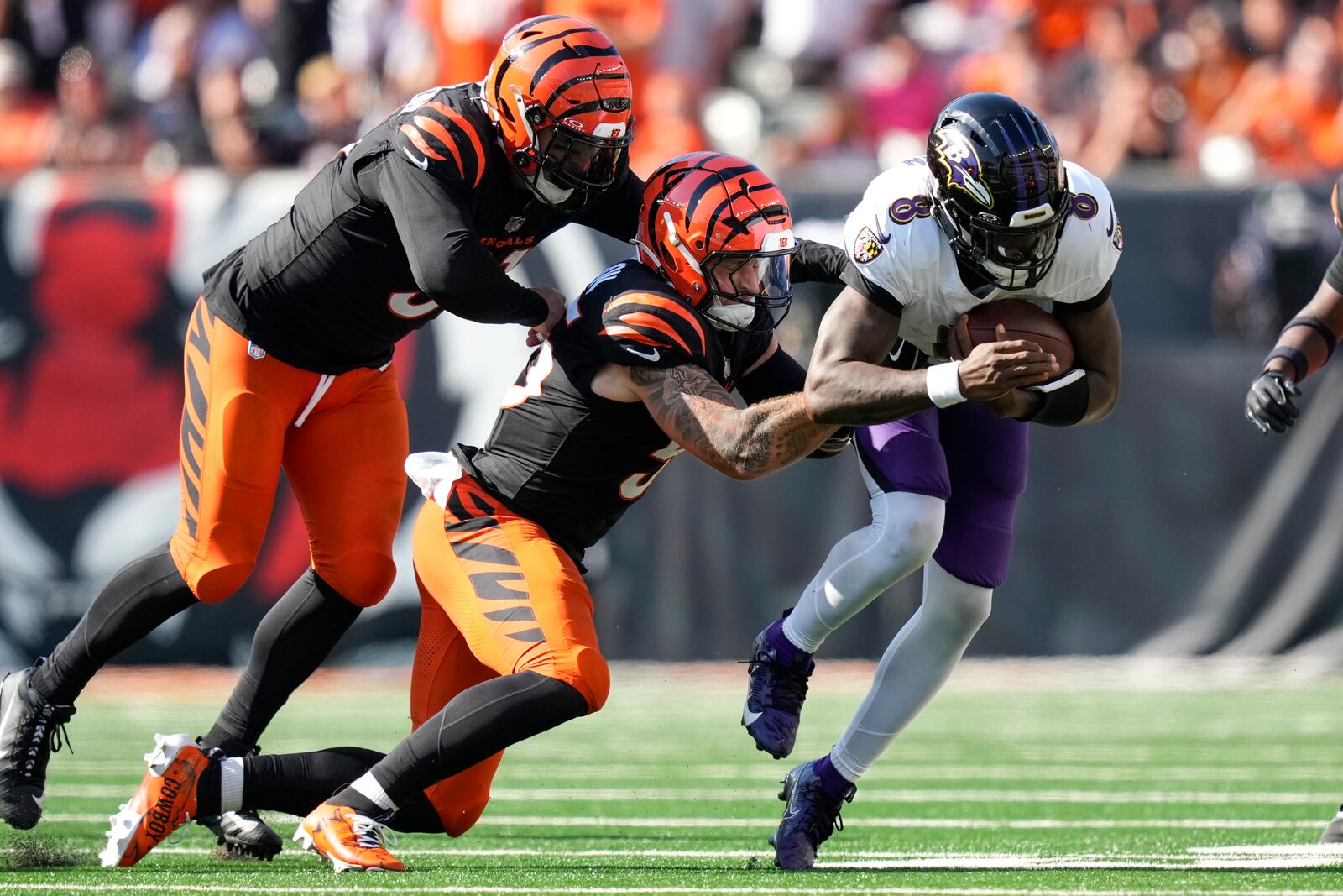 Baltimore Ravens quarterback Lamar Jackson=, right, runs with the ball as Cincinnati Bengals defensive end Trey Hendrickson, left, and linebacker Logan Wilson try to stop him during the second half of an NFL football game, Sunday, Oct. 6, 2024, in Cincinnati. (AP Photo/Carolyn Kaster)