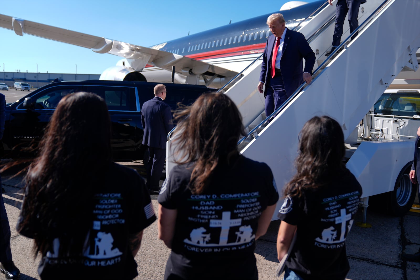 Republican presidential nominee former President Donald Trump arrives as family members of Corey Comperatore wait as he arrives at Pittsburgh International Airport en route to speak at a campaign rally at the Butler Farm Show, Saturday, Oct. 5, 2024, in Pittsburgh. (AP Photo/Evan Vucci)