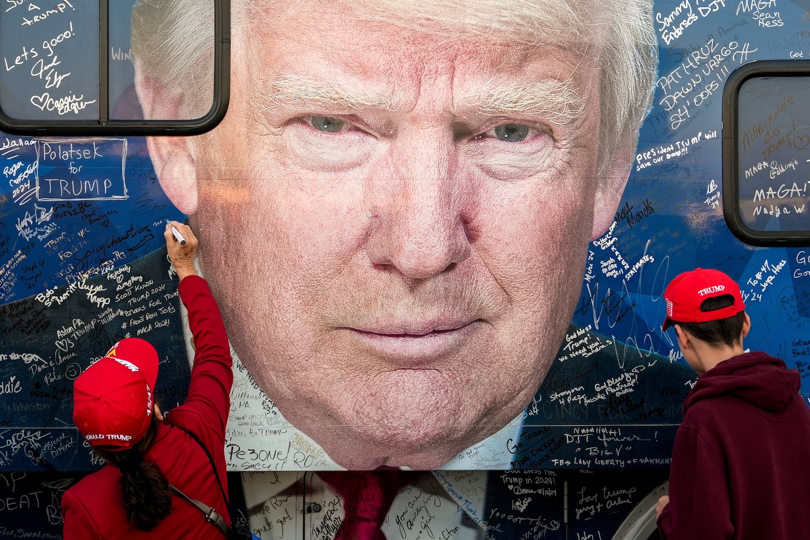 Supporters of Republican presidential nominee former President Donald Trump sign a bus before a campaign rally at the Butler Farm Show, Saturday, Oct. 5, 2024, in Butler, Pa. (AP Photo/Julia Demaree Nikhinson)