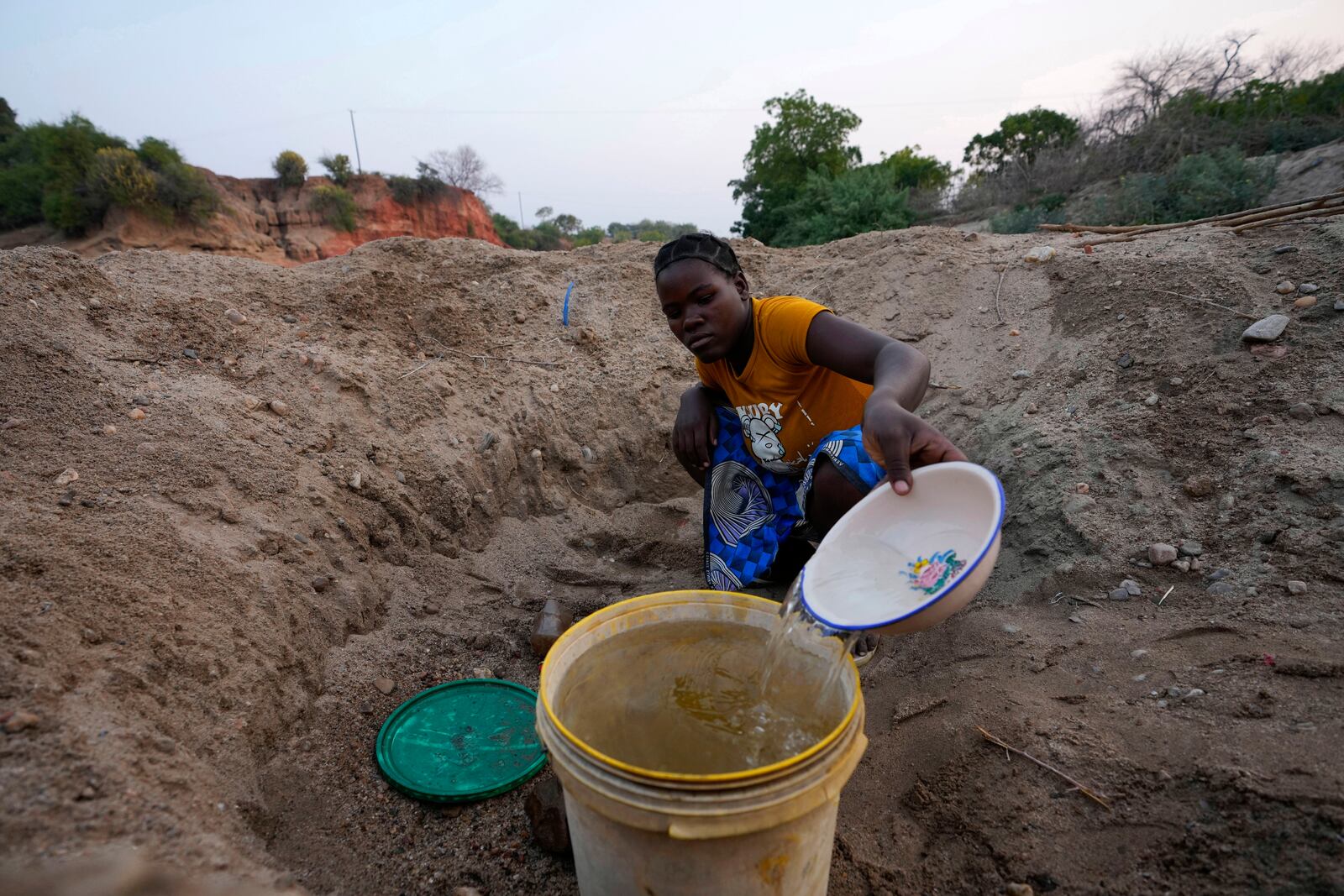 File — A woman scoops water from a hole she has dug in a dried up riverbed in Lusitu, Zambia, Wednesday, Sept. 18, 2024. (AP Photo/Themba Hadebe/File)