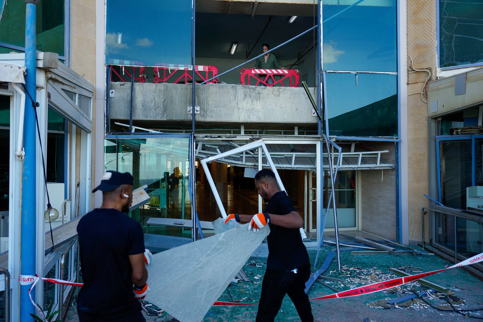 Workers remove broken glass from a damaged building that was hit during Iran's missile attack in Tel Aviv, Israel, Wednesday, Oct. 2, 2024. (AP Photo/Ariel Schalit)