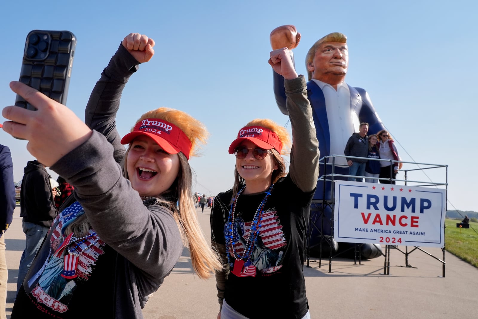 Faith Rail, right, and Kellie Kamphuis take a selfie in front of an inflatable of Republican presidential nominee former President Donald Trump before he speaks at a campaign stop at the Dodge County Airport Sunday, Oct. 6, 2024, in Juneau, Wis. (AP Photo/Morry Gash)