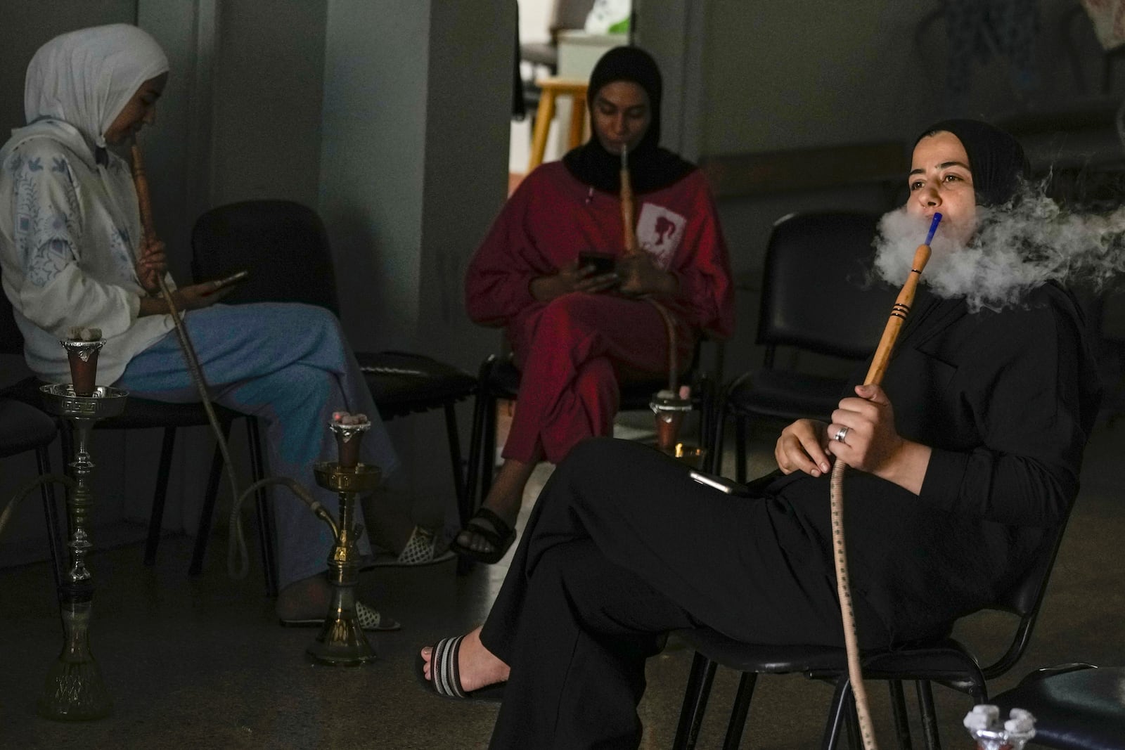 Displaced women smoke waterpipes as they sit in a school in Beirut, Thursday, Sept. 26, 2024. (AP Photo/Bilal Hussein)