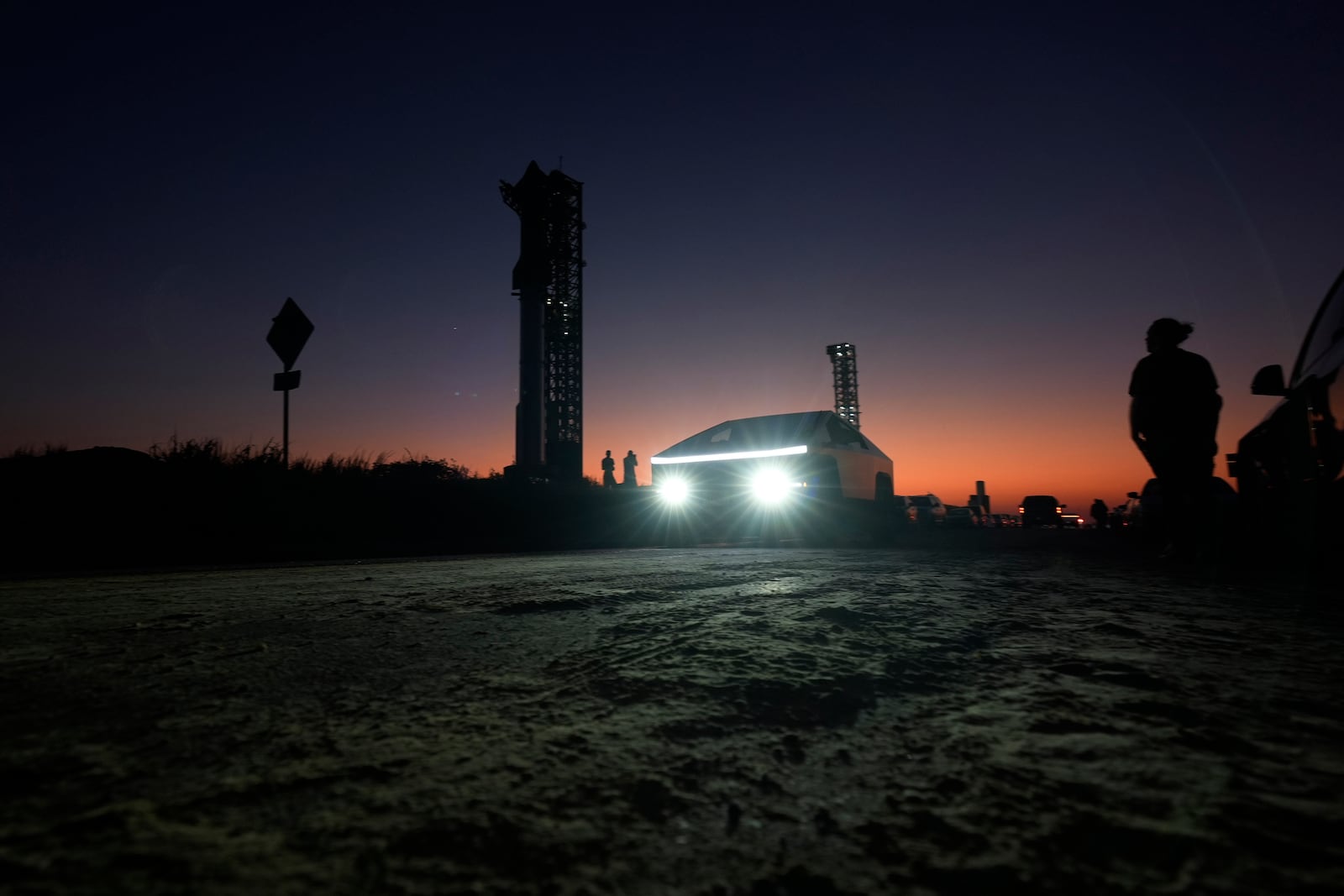 A Tesla Cybertruck passes as the sun sets behind SpaceX's mega rocket Starship, Saturday, Oct. 12, 2024, in Boca Chica, Texas. (AP Photo/Eric Gay)