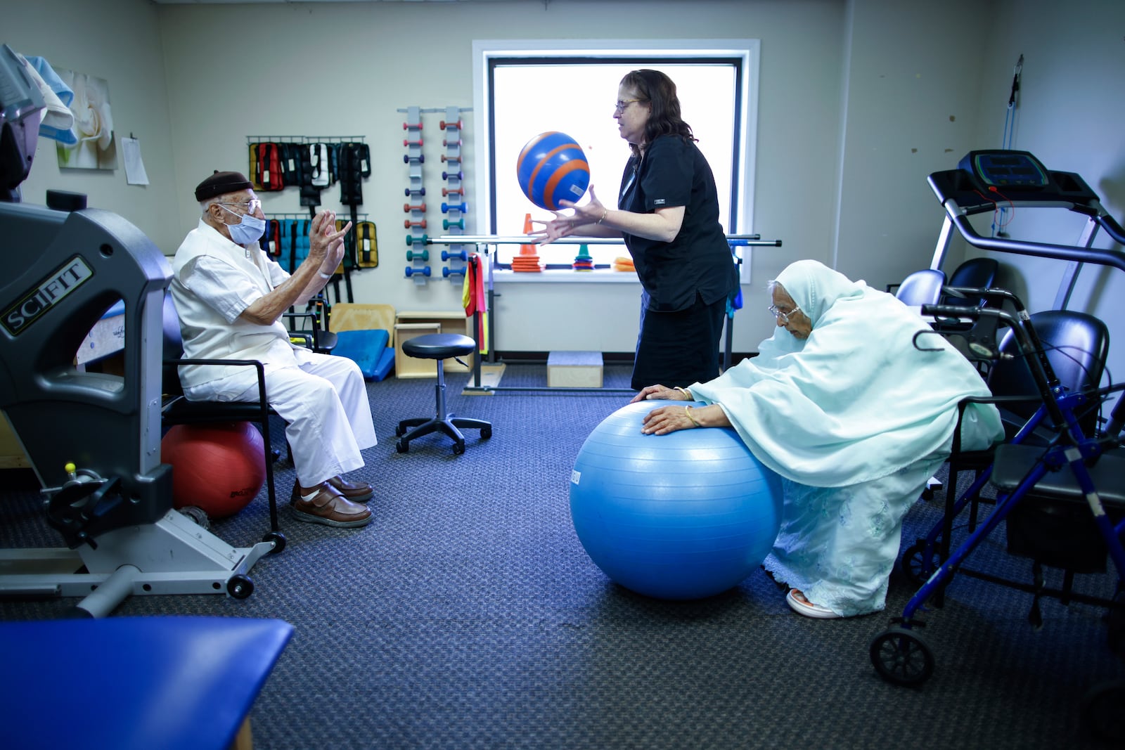 Mohamed, 84, left, receives physical therapy with therapist Susan Fenyes, center, while his wife, Bibi, 84, stretches with a ball at Sunshine Adult Day Center in Bergenfield, N.J., Monday, Aug. 26, 2024. (AP Photo/Kena Betancur)