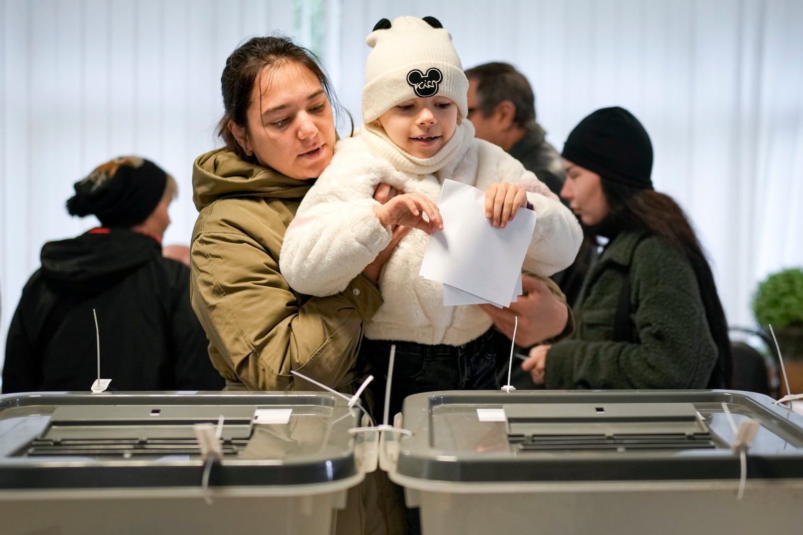 A woman holds a child as she casts her vote in Chisinau, Moldova, Sunday, Oct. 20, 2024, during a presidential election and a referendum on whether to enshrine in the Constitution the country's path to European Union membership. (AP Photo/Vadim Ghirda)