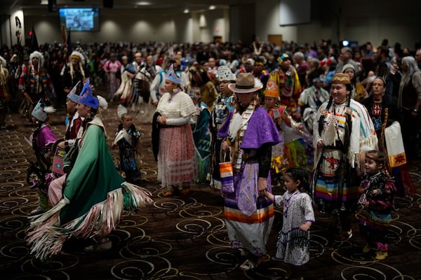 Tiffany Stuart, at right in white, holds hands with her daughter Kwestaani Chuski Stuart, bottom right, as they participate in a powwow at Chinook Winds Casino Resort, Saturday, Nov. 16, 2024, in Lincoln City, Ore. (AP Photo/Jenny Kane)