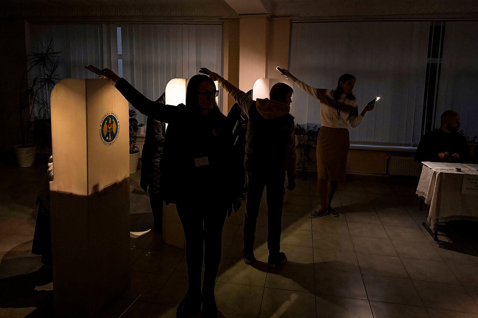 Election officials assist voters with mobile phone flashlights during a power failure in Chisinau, Moldova, Sunday, Oct. 20, 2024, during a presidential election and a referendum on whether to enshrine in the Constitution the country's path to European Union membership. (AP Photo/Nicolae Dumitrache)