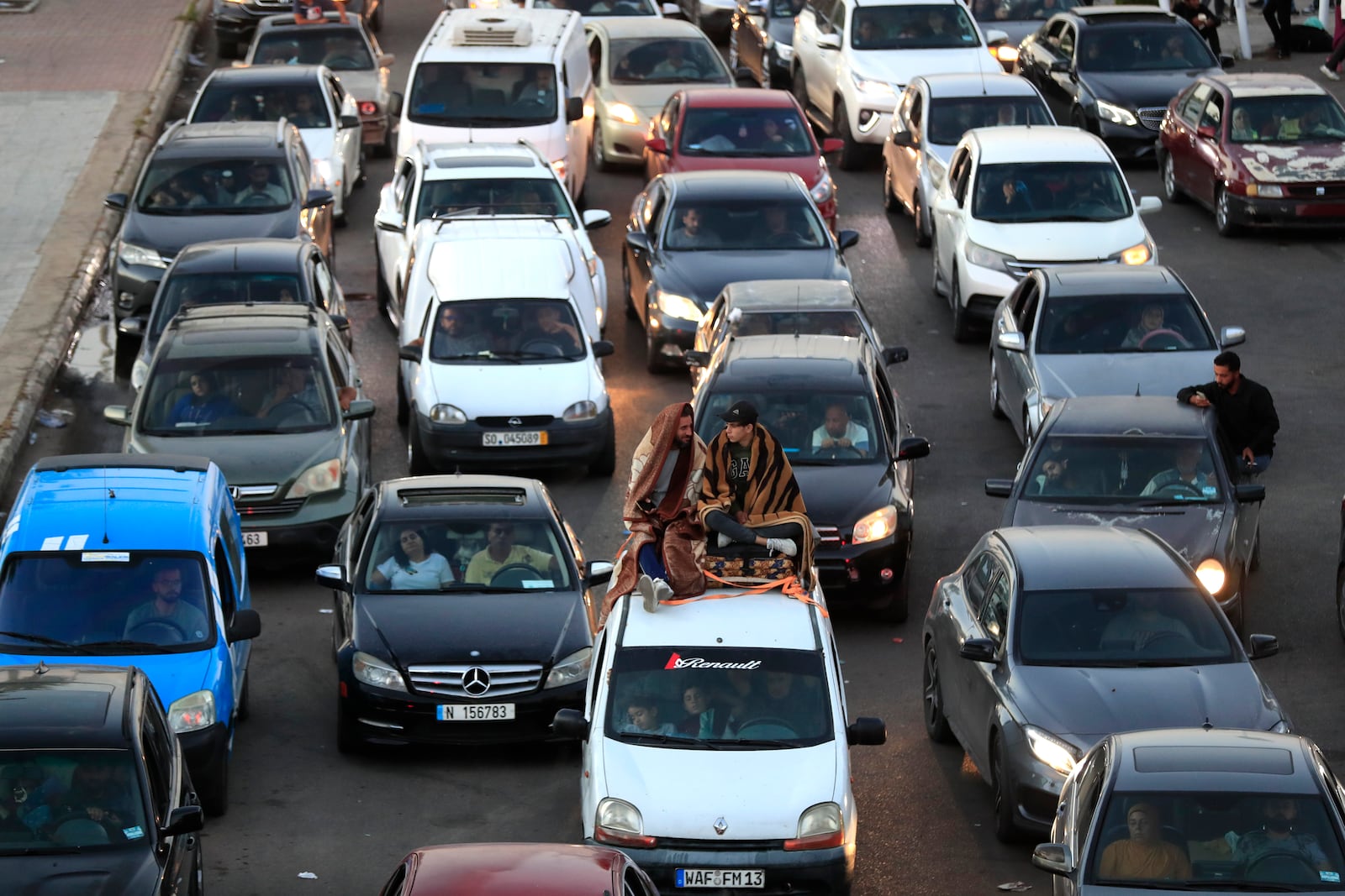 Lebanese citizens who fled the southern villages amid ongoing Israeli airstrikes Monday, sit on their cars at a highway that links to Beirut city, in the southern port city of Sidon, Lebanon, Tuesday, Sept. 24, 2024. (AP Photo/Mohammed Zaatari)