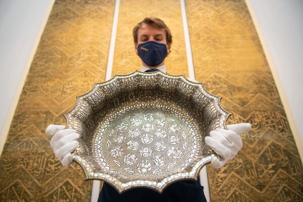 FILE - An employee at Sotheby's auction house holds a twelfth-century silver inlaid scalloped basin with astrological designs, estimated to fetch 1,000,000 - 1,500,000 sterling pounds, as part of the auction house's forthcoming Arts of the Islamic World and India sale on March 31, in London, March 29, 2021. (Dominic Lipinski/PA via AP)