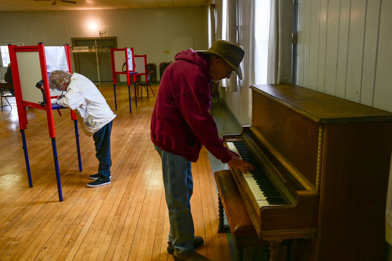 Charles Cunningham plays the piano as his mother Pearl votes at Drummond Community Hall in Drummond, Mont., on Election Day, Tuesday, Nov. 5, 2024. (AP Photo/Tommy Martino)