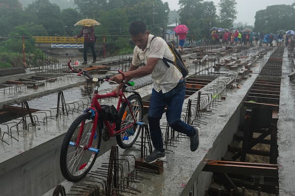 Residents cross a bridge under construction amid rain showers brought on by Tropical Storm Sara, on the outskirts of San Pedro Sula, Honduras, Saturday, Nov. 16, 2024. (AP Photo/Moises Castillo)