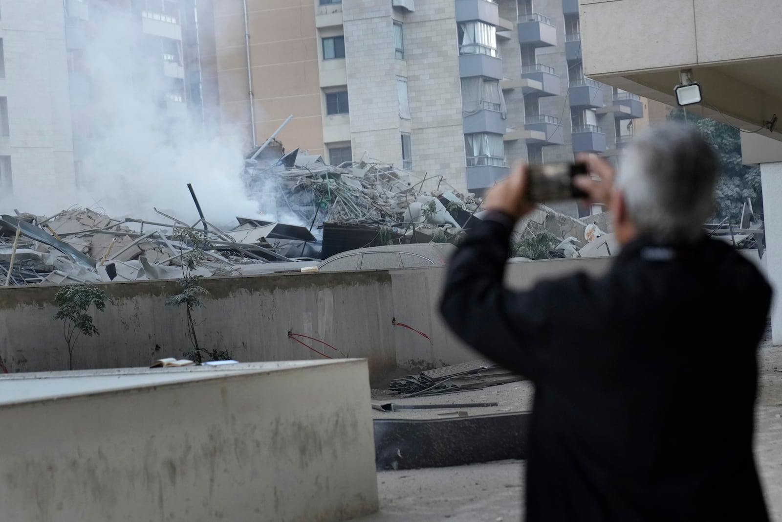 A man takes pictures with his mobile phone of a destroyed resident complex where he lives that hit by an Israeli airstrike in Dahieh, Beirut, Lebanon, Wednesday, Oct. 2, 2024. (AP Photo/Hussein Malla)