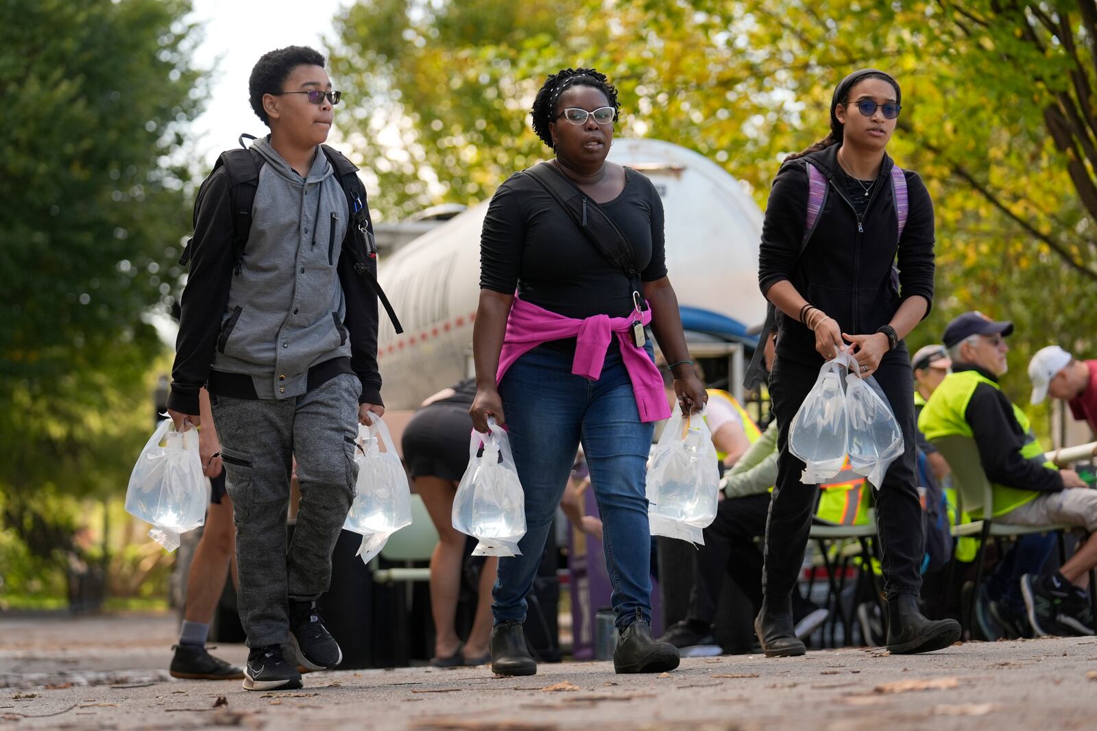 People carry bags of fresh water after filling up at a distribution site in the aftermath of Hurricane Helene Wednesday, Oct. 2, 2024, in Asheville, N.C. (AP Photo/Jeff Roberson)