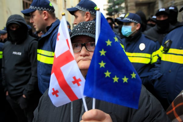 A woman with a EU and a Georgian national flags stands in front of police blocking a street during a rally to demand new parliamentary elections in the country, near the Parliament's building in Tbilisi, Georgia, on Monday, Nov. 25, 2024. (AP Photo/Shakh Aivazov)