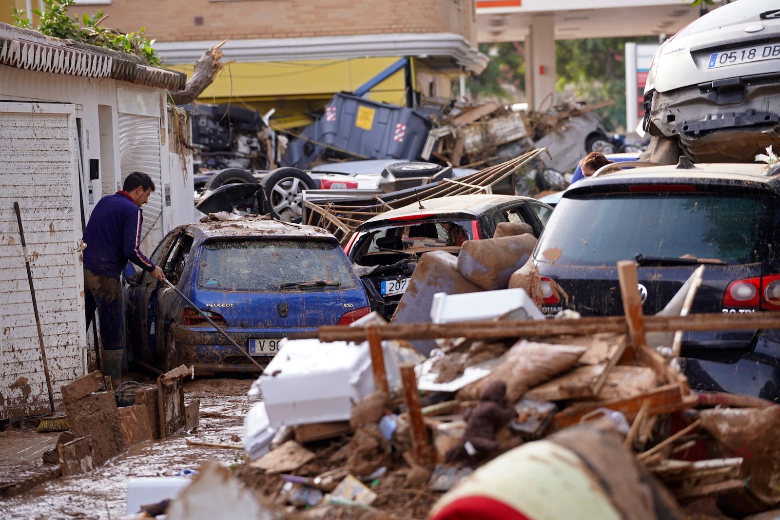 A man sweeps by piled up cars after floods in Massanassa, just outside of Valencia, Spain, Friday, Nov. 1, 2024. (AP Photo/Alberto Saiz)