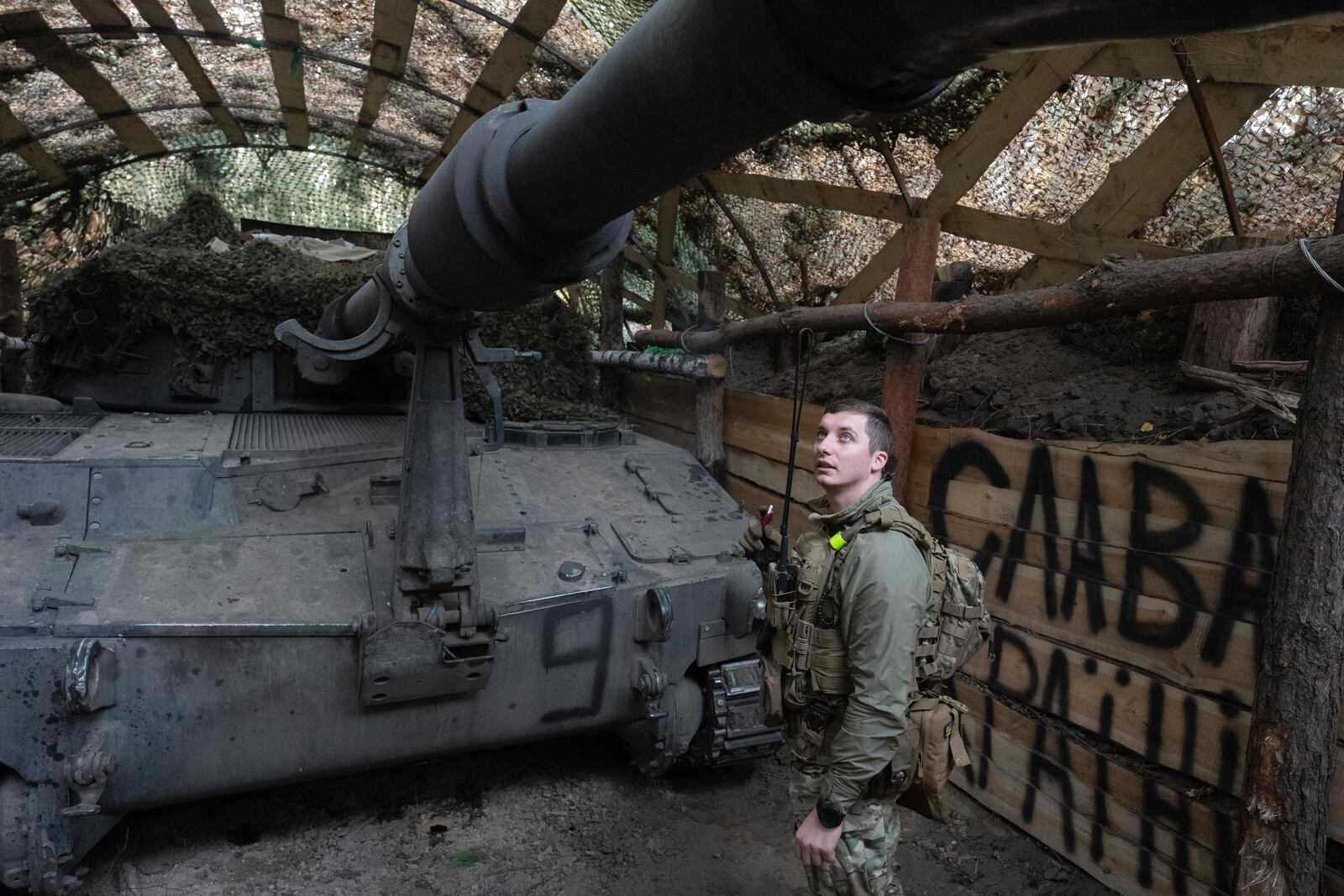 Ukrainian officer of the 92nd separate assault brigade inspects 155mm M-109 "Paladin" howitzer on the frontline near Vovchansk, Kharkiv region, Ukraine, Monday, Oct. 28, 2024, with the sign in the background reads "Glory to Ukraine". (AP Photo/Efrem Lukatsky)