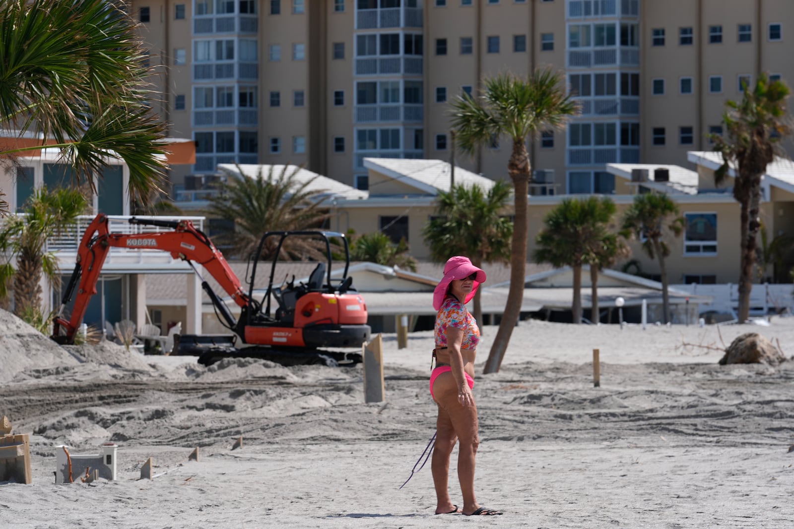 A condominium owner who says her unit, at the back of the property, was luckily undamaged, walks beside an almost-buried fence as she surveys the beginning of work to remove feet worth of extra sand from the beach and beachfront properties, in Venice, Fla.,following the passage of Hurricane Milton, Saturday, Oct. 12, 2024. (AP Photo/Rebecca Blackwell)