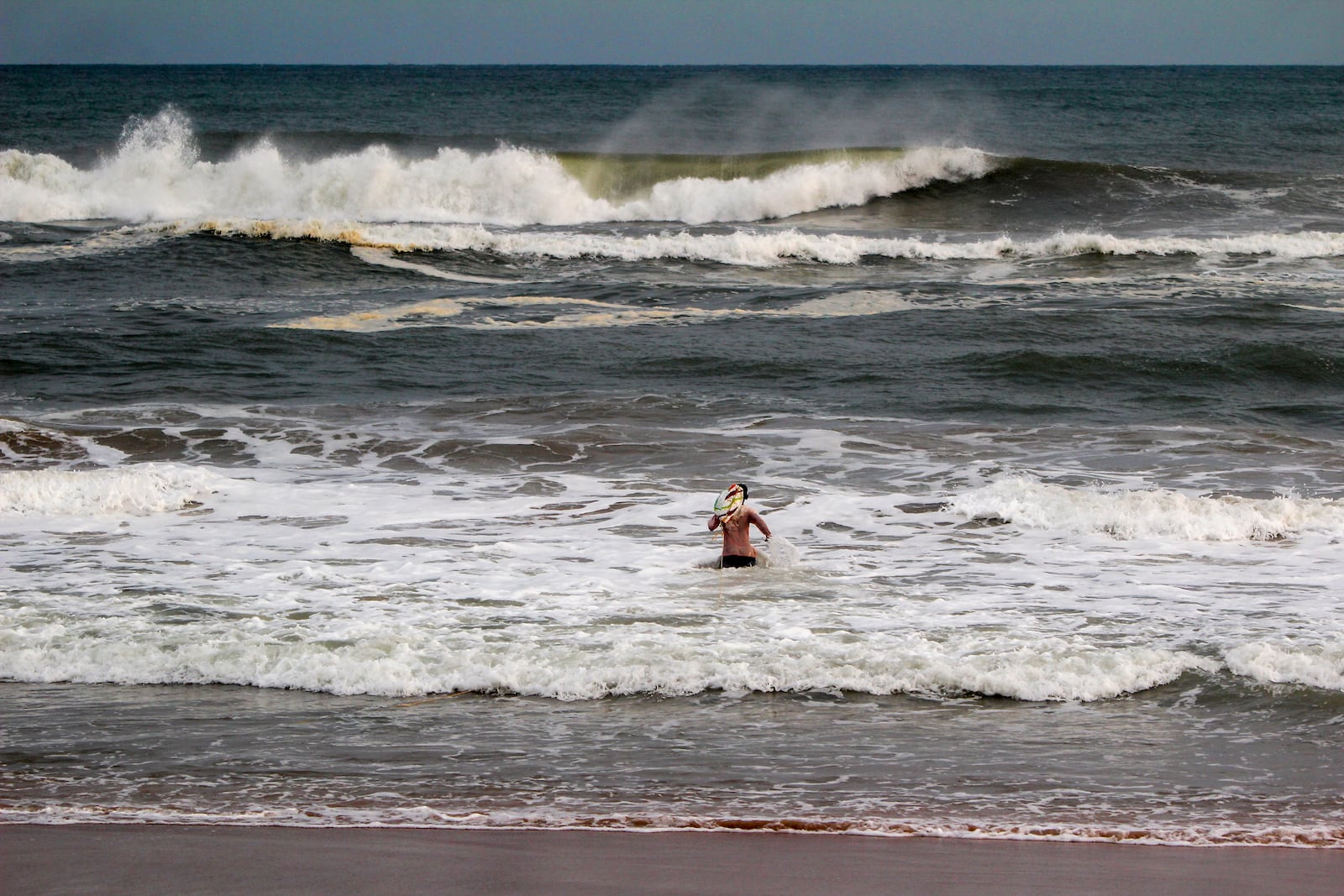 A surfer enters the Bay of Bengal at Konark beach in Puri district of Odisha state, on India's eastern coastline, where Tropical Storm Dana is expected to make landfall late on Thursday and early into Friday, according to the Indian Meteorological Department, India, Wednesday, Oct. 23, 2024. (AP Photo)