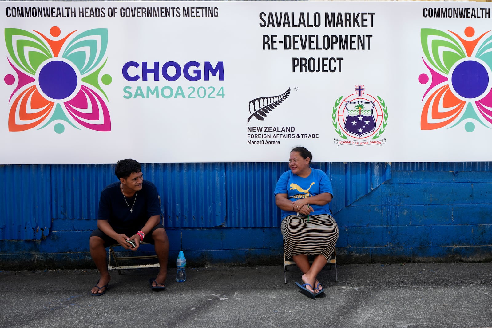 A man and woman rest in the shade of a Commonwealth Heads of Government banner in Apia, Samoa, on Monday, Oct. 21, 2024. (AP Photo/Rick Rycroft)