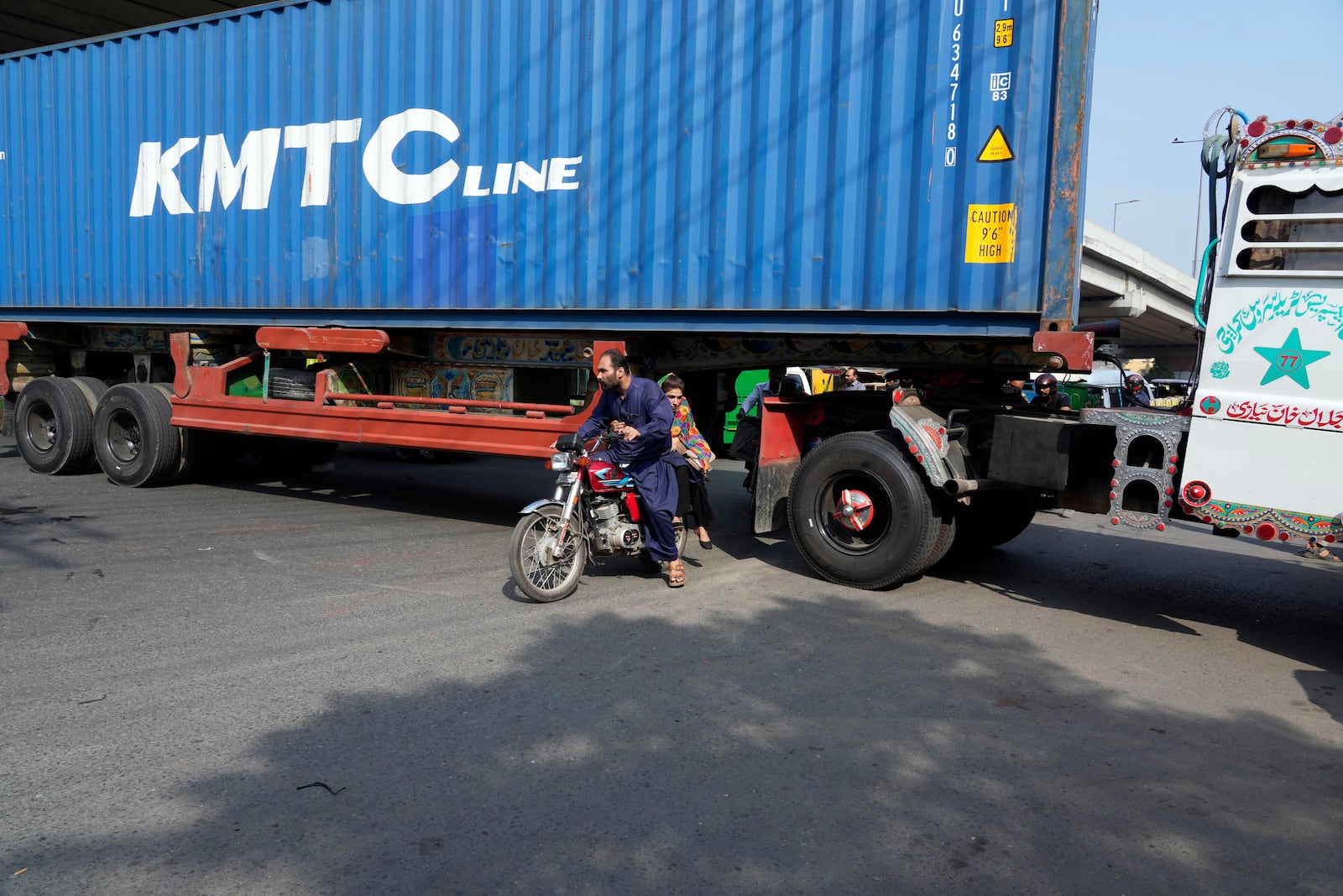 People try to cross through a shipping container placed by authorities to block the way to prevent supporters of imprisoned former Prime Minister Imran Khan from holding a rally in Lahore, Pakistan, Saturday, Oct. 5, 2024. (AP Photo/K.M. Chaudary)