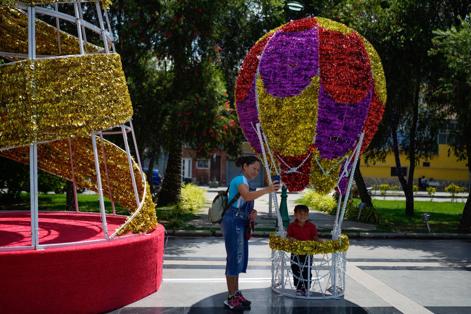 A woman takes a selfie with her daughter inside a Christmas decoration in Caracas, Venezuela, Tuesday, Oct. 1, 2024. (AP Photo/Ariana Cubillos)