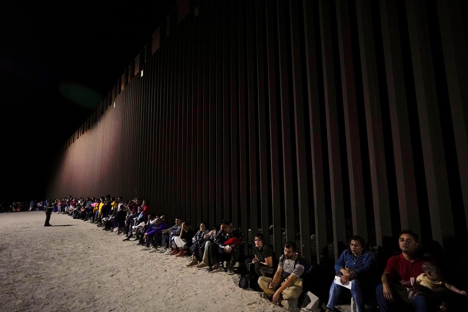 FILE - Migrants wait to be processed after crossing into the United States near the end of a border wall, on Aug. 23, 2022, near Yuma, Ariz. (AP Photo/Gregory Bull)