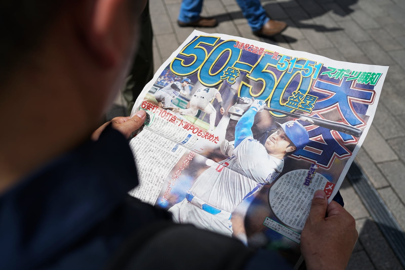 A pedestrian reads an extra edition of the Sports Hochi newspaper reporting on the Los Angeles Dodgers' Shohei Ohtani becoming the first player in major league history with 50 home runs and 50 stolen bases in a season, Friday, Sept. 20, 2024, in Tokyo. (AP Photo/Eugene Hoshiko)