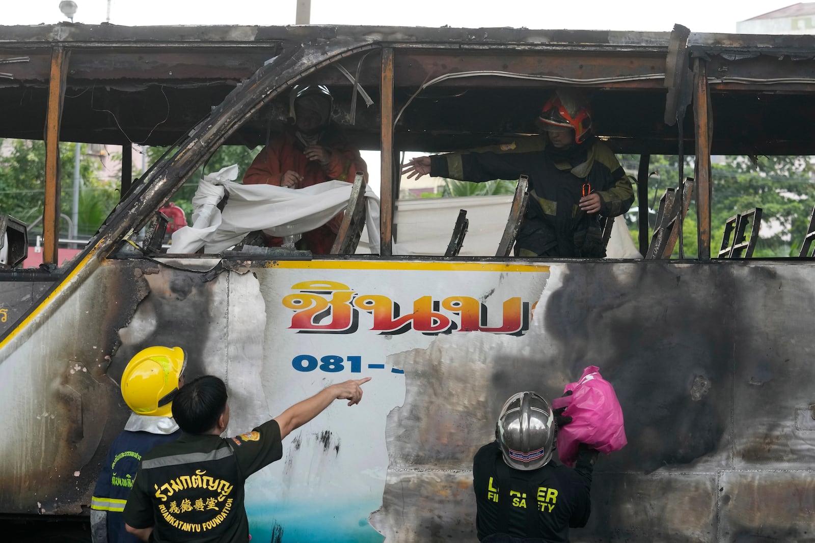 Rescuers hold a white cloth to cover the body of a victim inside a bus that caught fire, carrying young students with their teachers, in suburban Bangkok, Tuesday, Oct. 1, 2024. (AP Photo/Sakchai Lalit)