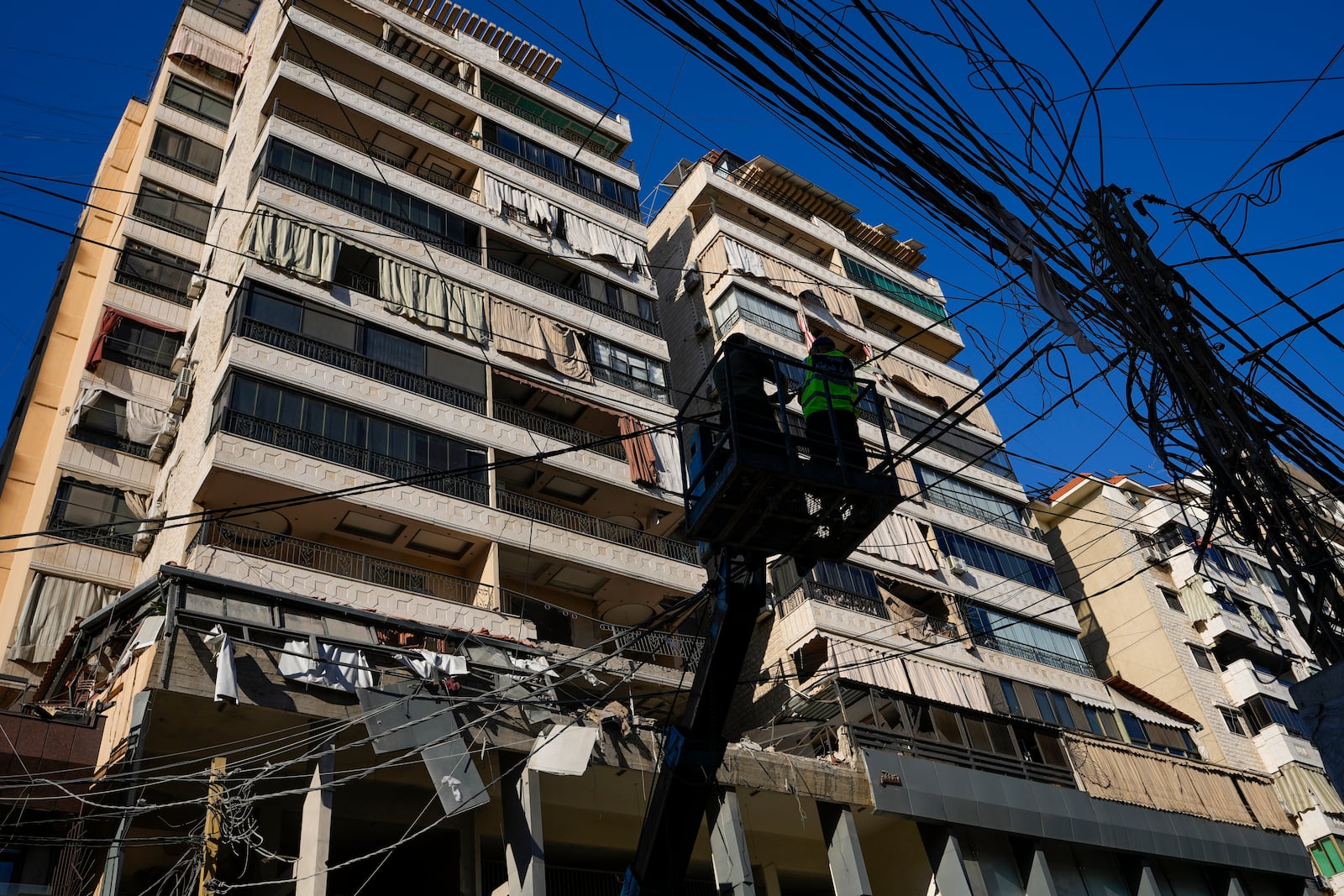 Municipality workers remove power cables in front of damaged buildings at the site of an Israeli airstrike in Beirut's southern suburb, Thursday, Sept. 26, 2024. (AP Photo/Hassan Ammar)