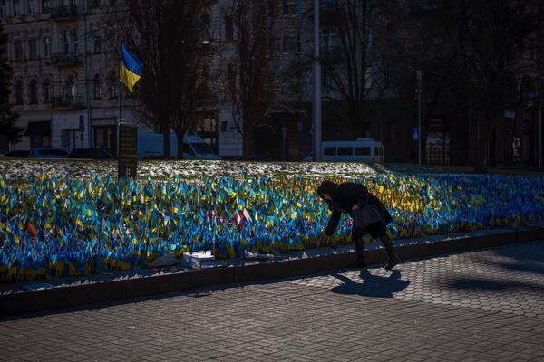 A woman places a Ukrainian flag at a memorial for those killed during the war in Independence Square in Kyiv, Ukraine, Sunday, Feb. 12, 2023. (AP Photo/Emilio Morenatti)