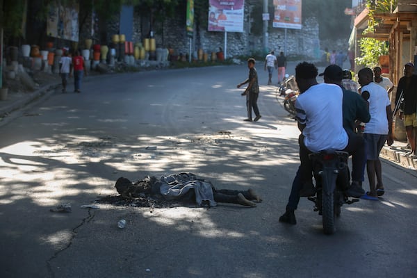 Passersby look at the abandoned body of an alleged gang member who was set on fire by residents, in the Pétion-Ville neighborhood of Port-au-Prince, Haiti, Tuesday, Nov. 19, 2024. (AP Photo/Odelyn Joseph)