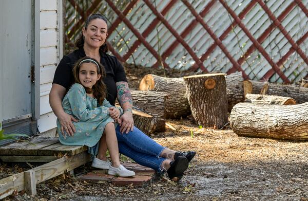 Cecila Grove and her daughter Aria Grove sit outside their home Saturday, Nov. 16, 2024, in Sarasota, Fla., next to limbs from a tree that fell durring the recent hurricanes. (AP Photo/Steve Nesius)