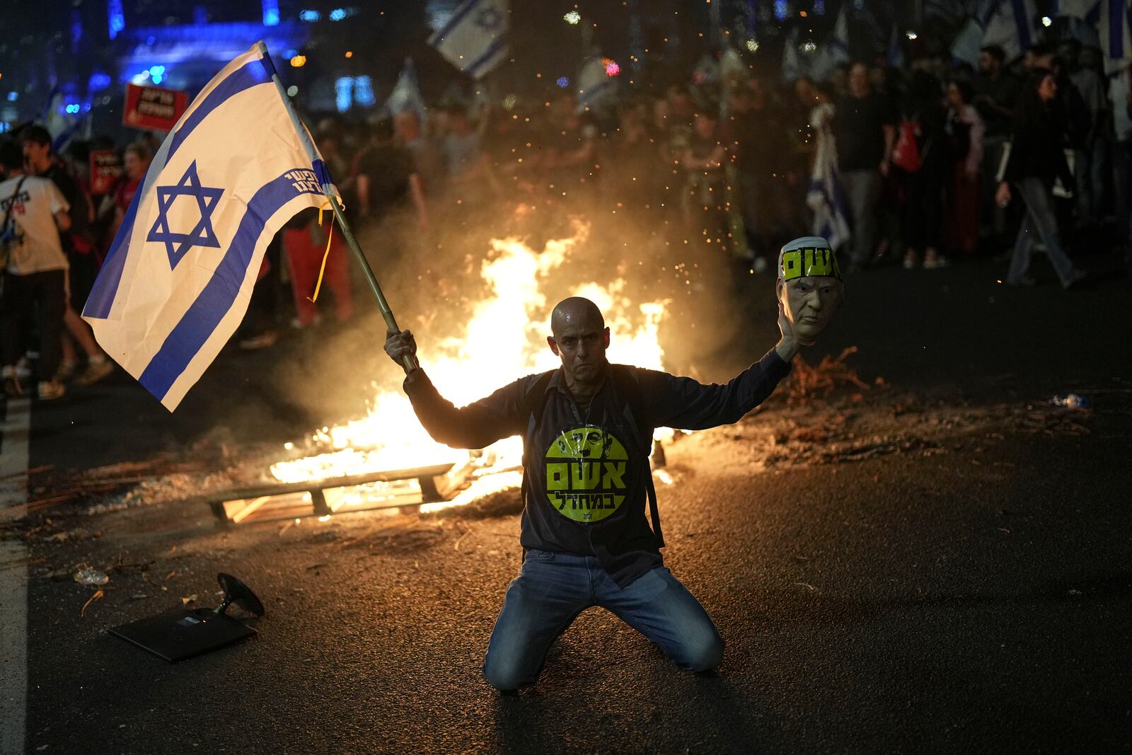 A protester holds an Israeli flag as Israelis light a bonfire during a protest after Prime Minister Benjamin Netanyahu has dismissed his defense minister Yoav Gallant in a surprise announcement in Tel Aviv, Israel, Tuesday, Nov. 5, 2024. (AP Photo/Francisco Seco)