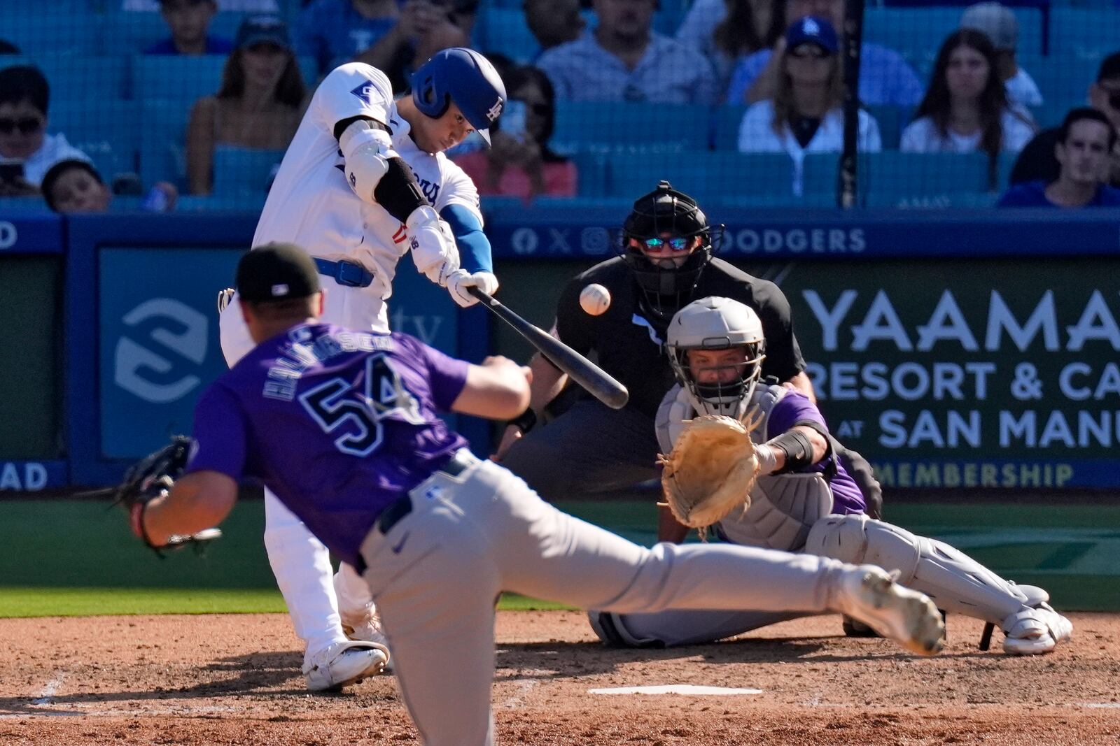 Los Angeles Dodgers' Shohei Ohtani, second from left, hits a solo home run as Colorado Rockies relief pitcher Seth Halvorsen, left, watches along with catcher Jacob Stallings, right, and home plate umpire Alex MacKay during the ninth inning of a baseball game, Sunday, Sept. 22, 2024, in Los Angeles. (AP Photo/Mark J. Terrill)