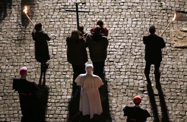 FILE - Pope Benedict XVI, in white at center, stands still on the cobblestone pavement behind a family carrying a wooden cross, during the Via Crucis (Way of the Cross) torchlight procession celebrated by the pontiff on Good Friday at the ancient Colosseum in Rome, April 6, 2007. (AP Photo/Pier Paolo Cito, File)