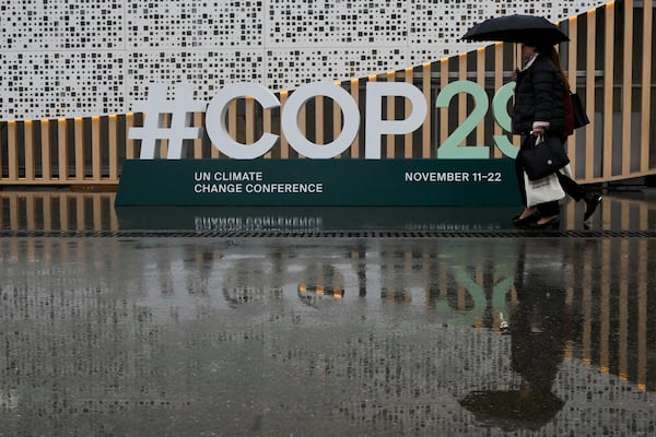 People arrive as it rains at the COP29 U.N. Climate Summit, Monday, Nov. 18, 2024, in Baku, Azerbaijan. (AP Photo/Rafiq Maqbool)