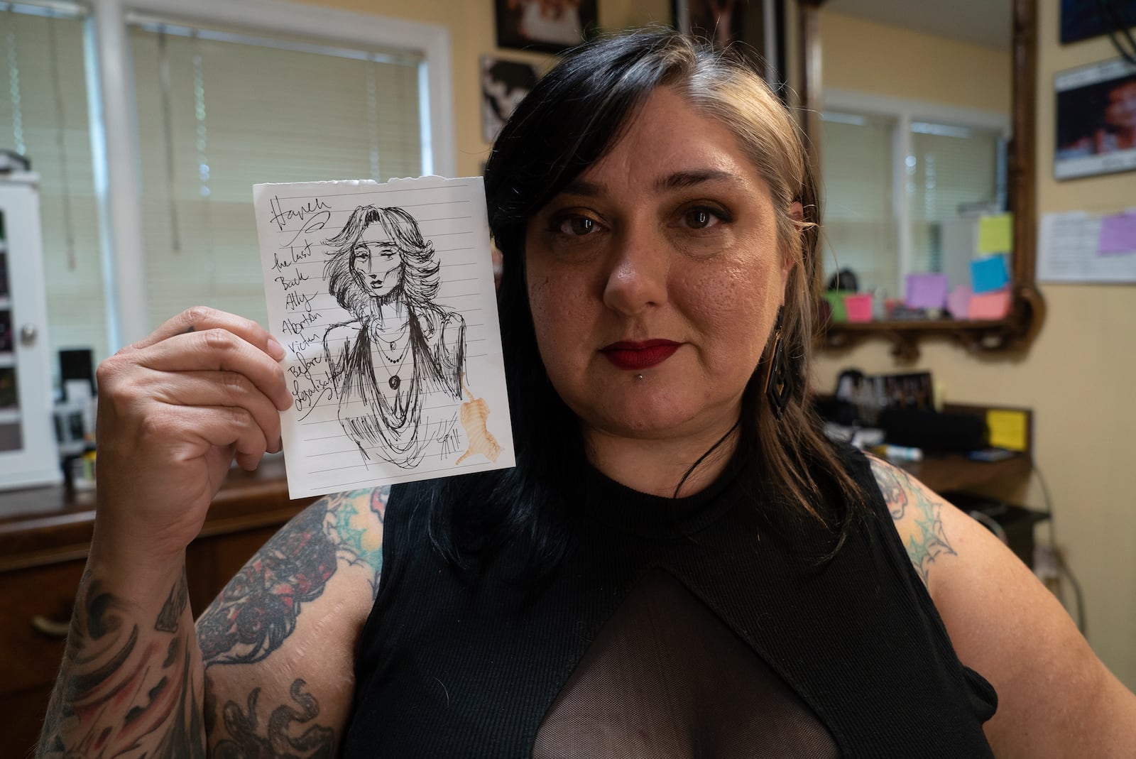 Tattoo artist Liz "Gruesome" Haycraft poses with a drawing of a fictitious back-alley abortion victim at her Breathless Arts Tattoo studio in Fayetteville, N.C., on Monday, Sept. 30, 2024. Haycraft drew it the day the U.S. Supreme Court overturned Roe v. Wade, which had previously legalized abortion nationwide. (AP Photo/Allen G. Breed)