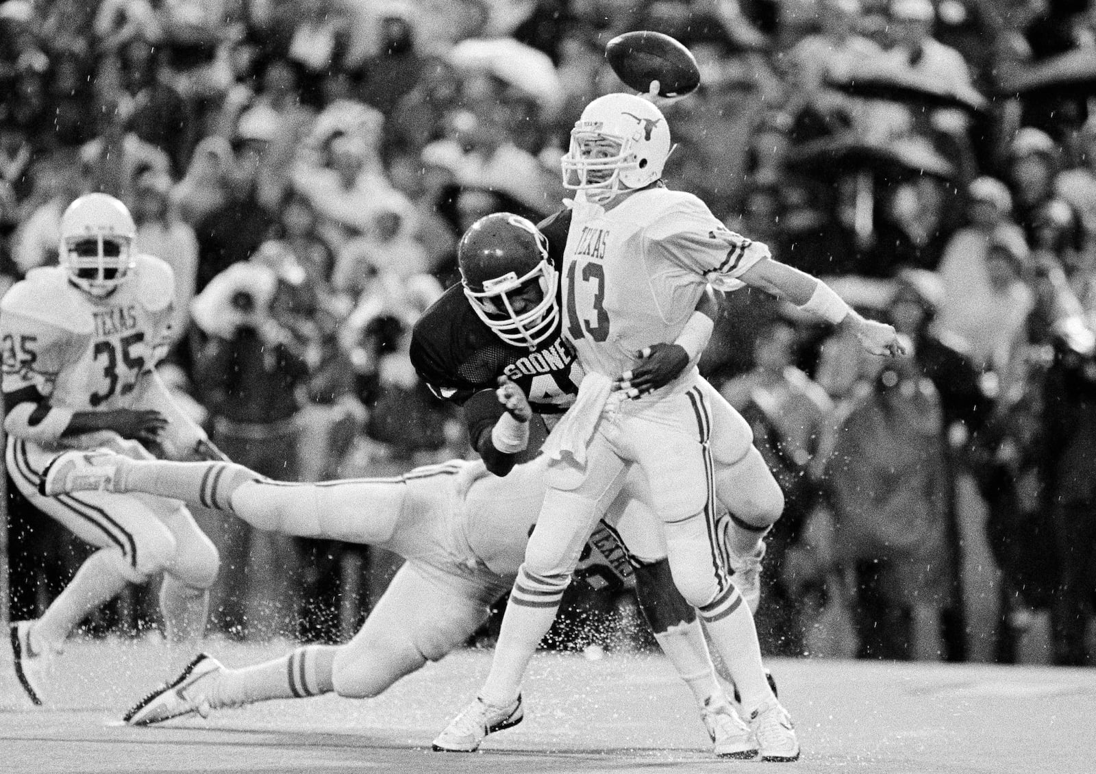 FILE - In this Oct. 13, 1984, file photo, Texas quarterback Todd Dodge (13) gets the ball away as he is tackled by Oklahoma's Darell Reed (40) during the third period of an NCAA college football game in Dallas. The pass fell incomplete. The game ended in a 15-15 tie. (AP Photo/Ron Ennis, File)