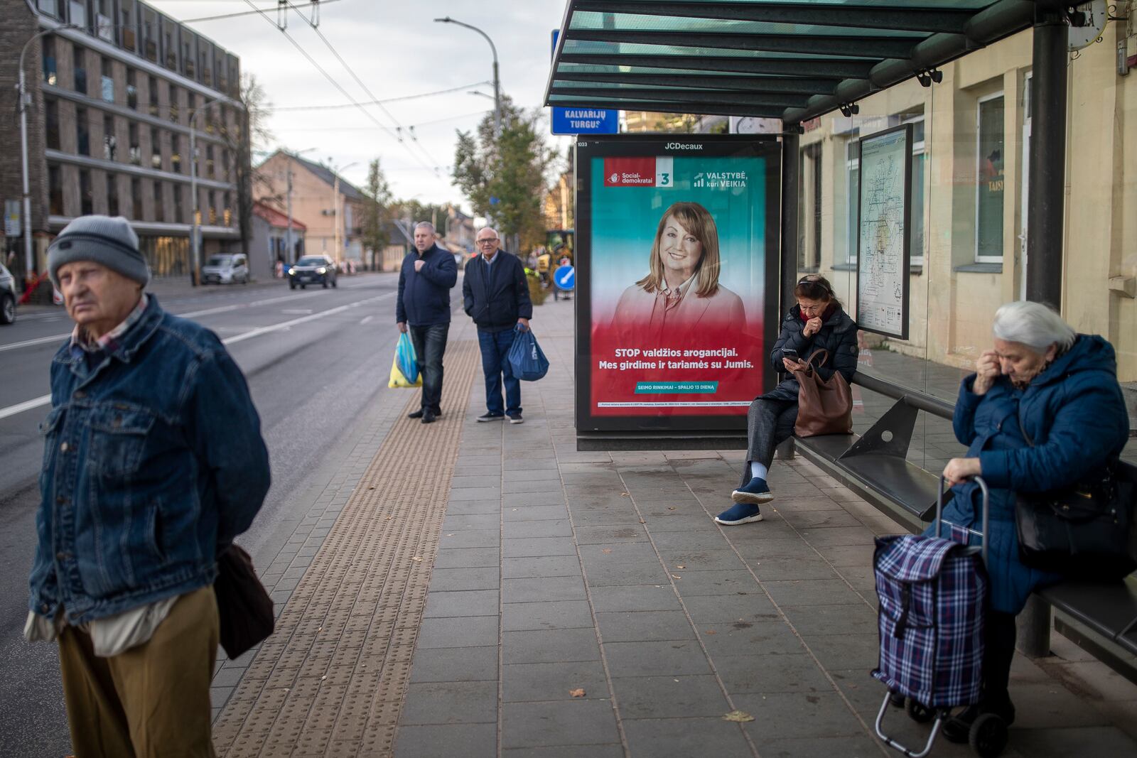 Local residents wait at a bus stop, with a poster displaying leader of the Social Democratic Party Vilija Blinkeviciute in Vilnius, Lithuania, Wednesday, Oct. 9, 2024. (AP Photo/Mindaugas Kulbis)