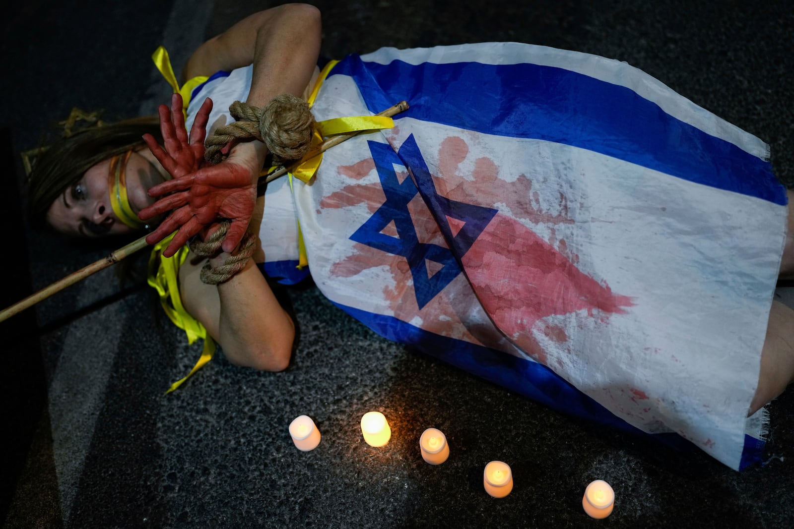 A demonstrator is painted red, symbolizing blood, during a protest calling for the immediate release of hostages held by Hamas militants in the Gaza Strip, in Tel Aviv, Israel, Saturday, Oct. 26, 2024. (AP Photo/Tsafrir Abayov)