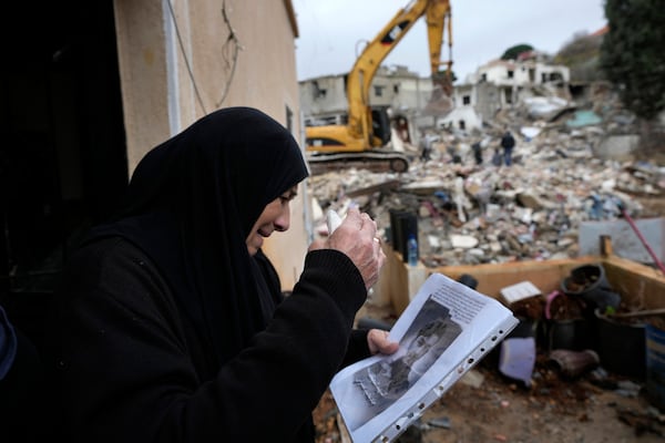 A woman mourns holding a portrait of her grandson, a Hezbollah fighter who was killed in the fighting with Israeli troops, as she waits for rescuers to recover his body from under the rubble of a destroyed house, background, in Ainata village, south Lebanon, following a ceasefire between Israel and Hezbollah on Wednesday, Nov. 27, 2024. (AP Photo/Hussein Malla)