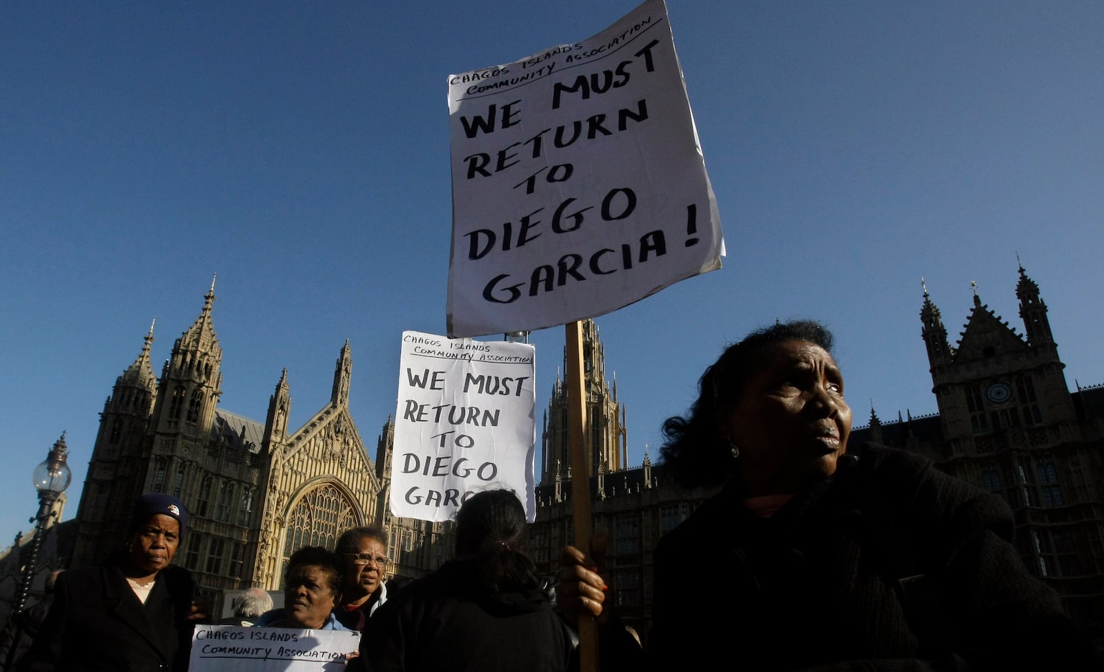 FILE - Women take part in a protest outside the Houses of Parliament in London, after a court ruling decided Chagos Islanders were not allowed to return to their homeland, Oct. 22, 2008. (AP Photo/Matt Dunham, file)