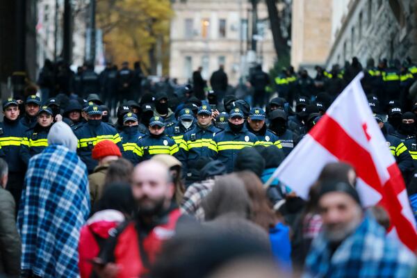 Protesters with a Georgian national flag stand in front of police blocking the entrance of the Parliament's building during a rally to demand new parliamentary elections in the country, in Tbilisi, Georgia, Monday, Nov. 25, 2024. (AP Photo/Zurab Tsertsvadze)