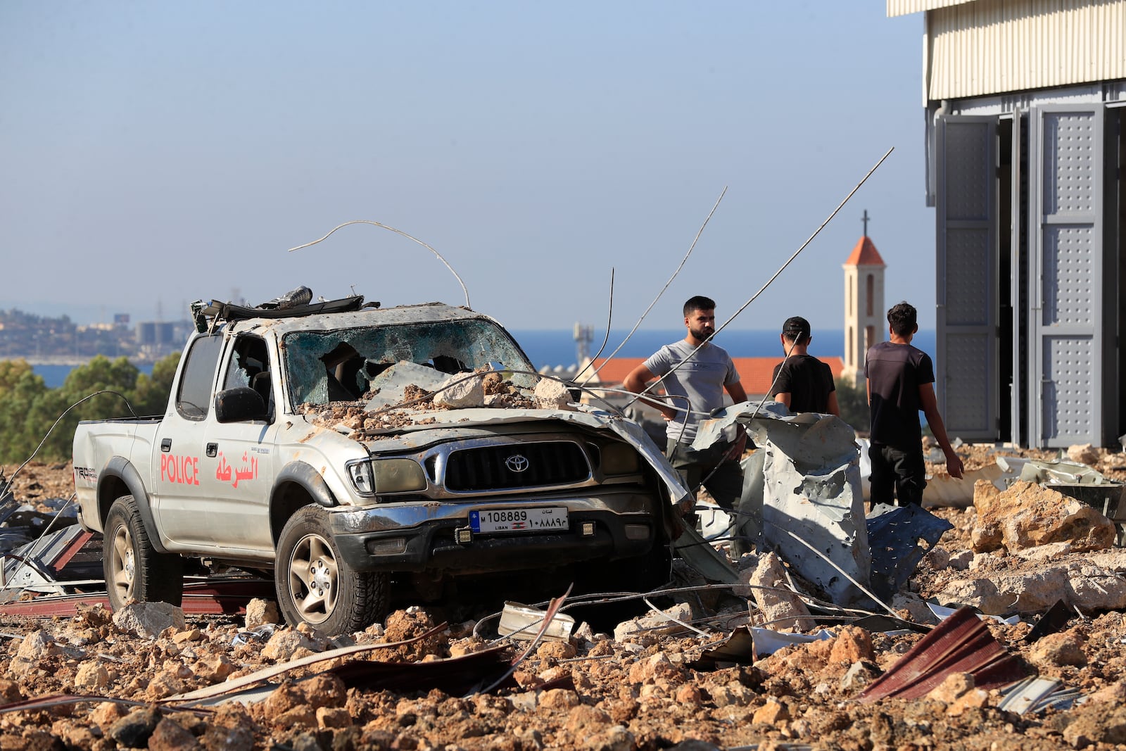 People gather near a damaged car at the site of an Israeli airstrike that hit a hangar in the southern town of Jiyeh, Lebanon, Wednesday, Sept. 25, 2024. (AP Photo/Mohammed Zaatari)