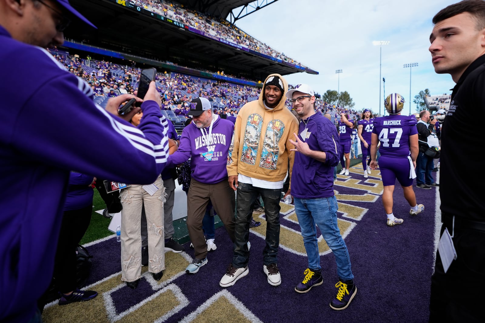 Former Washington quarterback Michael Penix Jr., in gold, takes photos with fans before an NCAA college football game against Michigan, Saturday, Oct. 5, 2024, in Seattle. (AP Photo/Lindsey Wasson)