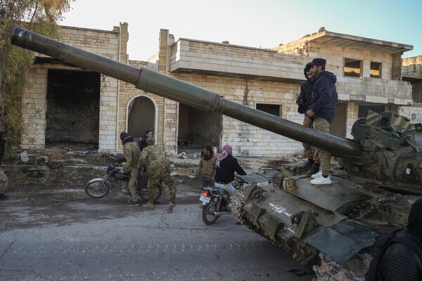 Syrian opposition fighters get on a motorcycle as opposition supporters stand on top of a captured army armoured vehicle in the town of Maarat al-Numan, southwest of Aleppo, Syria, Saturday Nov. 30, 2024. Thousands of Syrian insurgents have fanned out inside Syria's largest city Aleppo and large areas around previously controlled by the government with little resistance from troops.(AP Photo/Omar Albam)