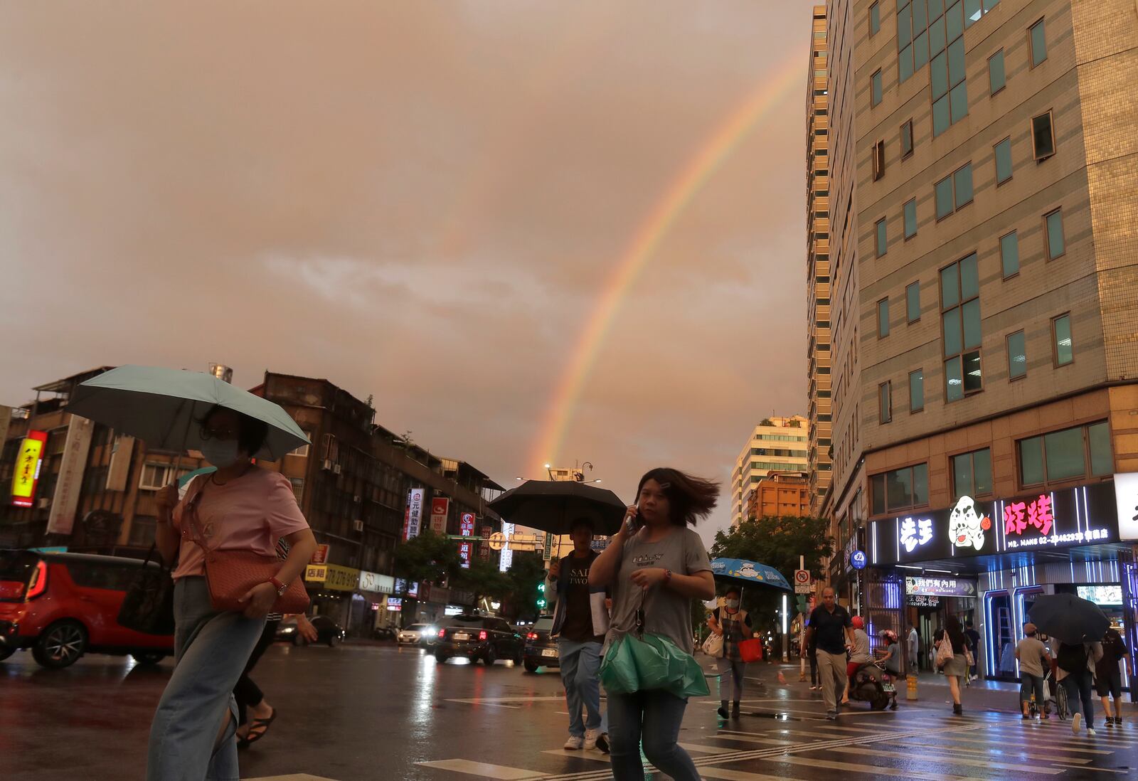 People walk in the rain with a backdrop of the rainbow in the sky as Typhoon Krathon approaches to Taiwan in Taipei, Monday, Sept. 30, 2024. (AP Photo/Chiang Ying-ying)